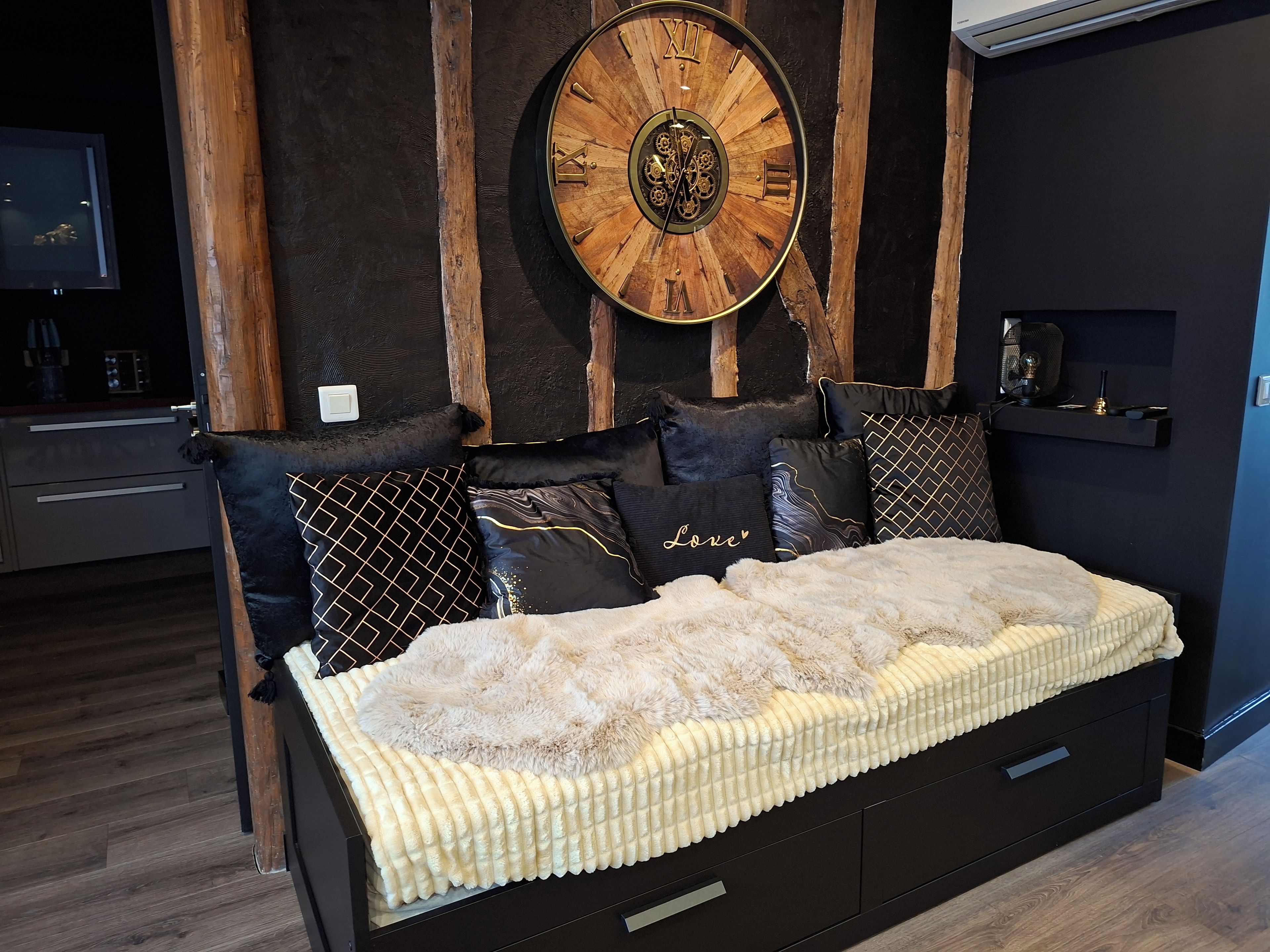 Une chambre à coucher moderne avec une tête de lit en bois, une grande horloge murale et un lit recouvert d’une couette blanche et moelleuse.