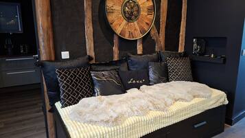 Une chambre à coucher moderne avec une tête de lit en bois, une grande horloge murale et un lit recouvert d’une couette blanche et moelleuse.