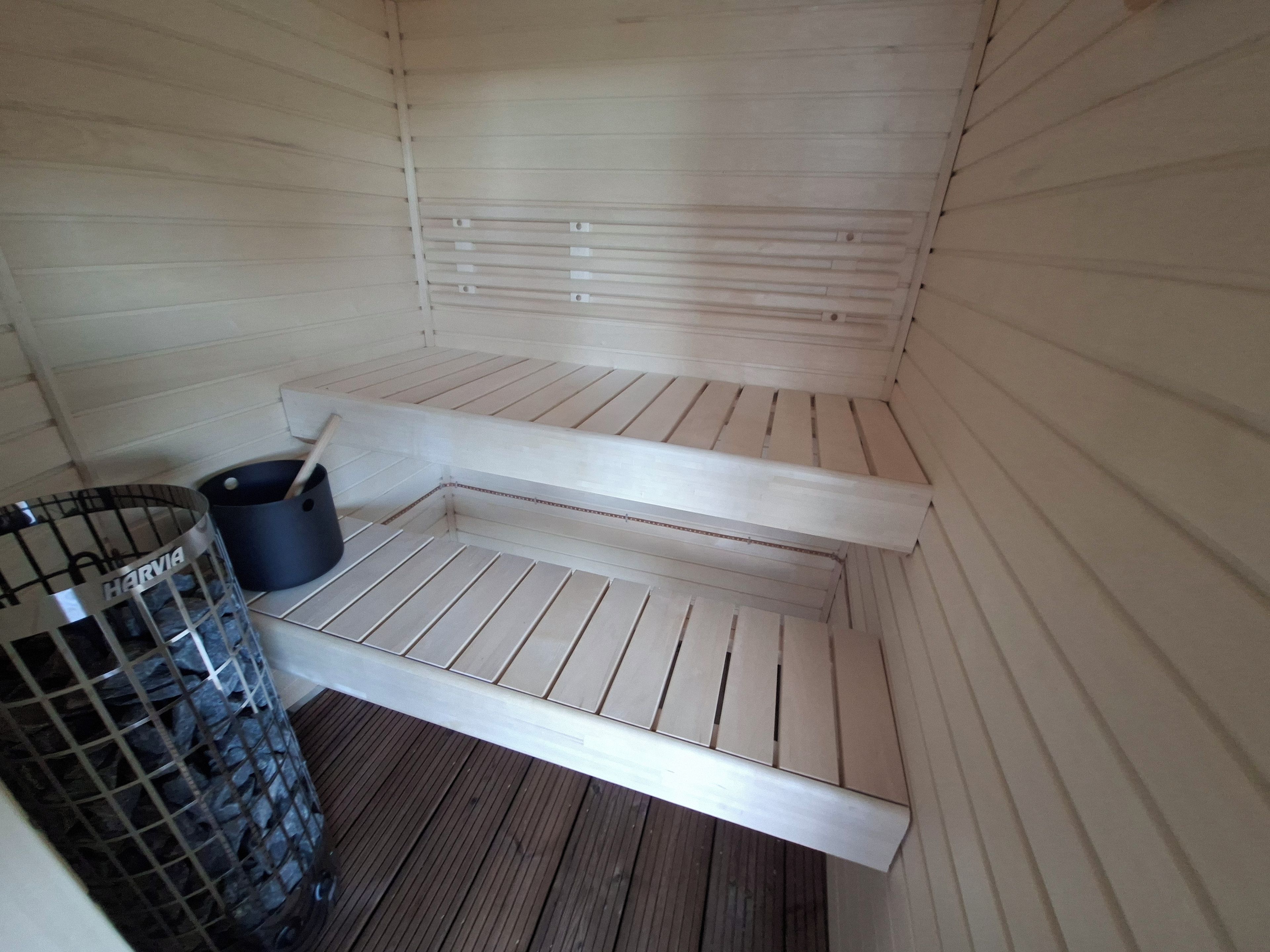 Een sauna met een bank, een metalen bak en een houten vloer.