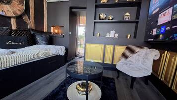 Een moderne woonkamer met een bank, een glazen salontafel en een aan de muur bevestigde televisie.
