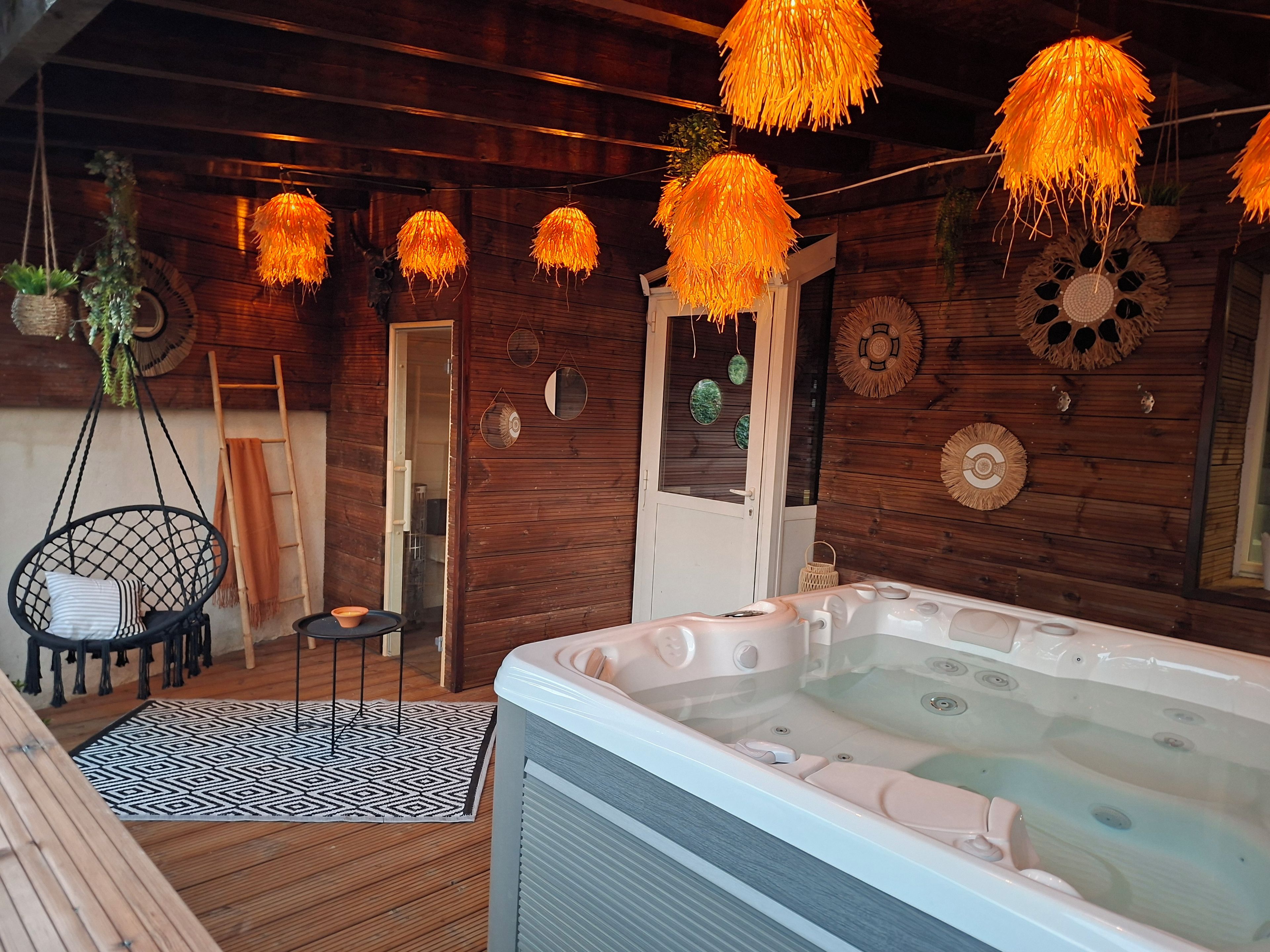 Interior de una cabaña de madera con un jacuzzi, lámparas colgantes y una mecedora.