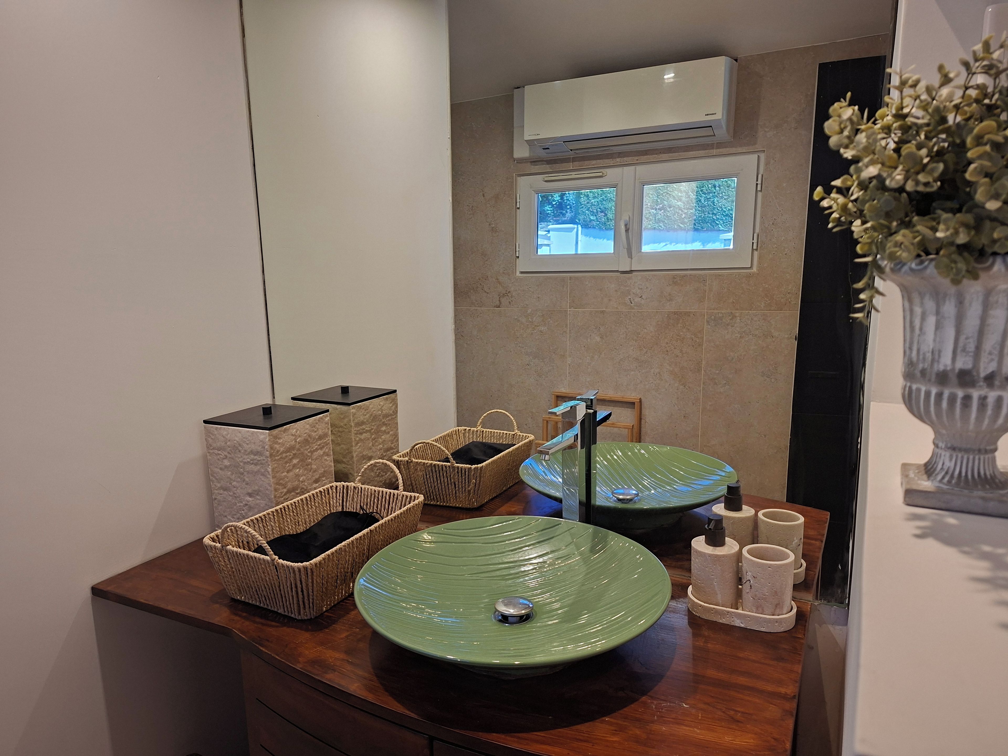 A bathroom with a green sink, wicker baskets, a mirror, and an air conditioning unit.