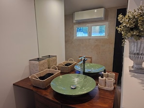 A bathroom with a green sink, wicker baskets, a mirror, and an air conditioning unit.