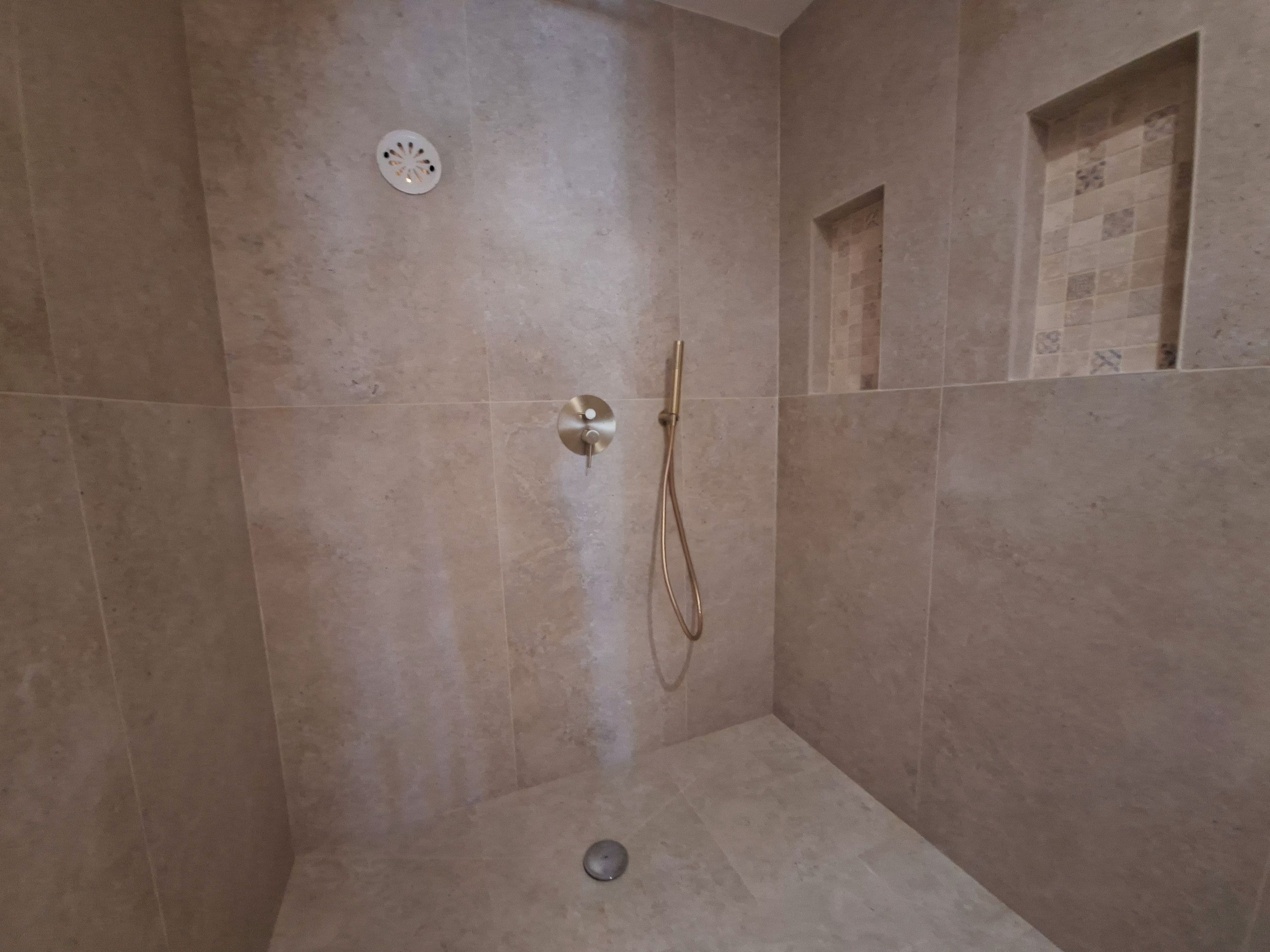Een douche met een handdouche en bediening aan de muur.
