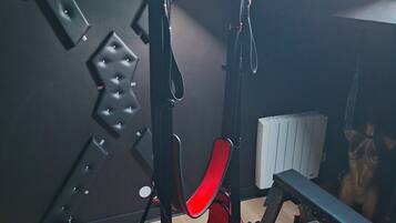 Una habitación con un sistema de suspensión para ejercicios instalado en el techo, un radiador y un banco de madera.