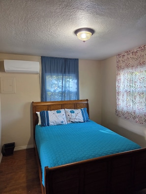 Une chambre à coucher avec un lit, une fenêtre ornée de rideaux à motifs floraux, un appareil de climatisation et un luminaire au plafond.