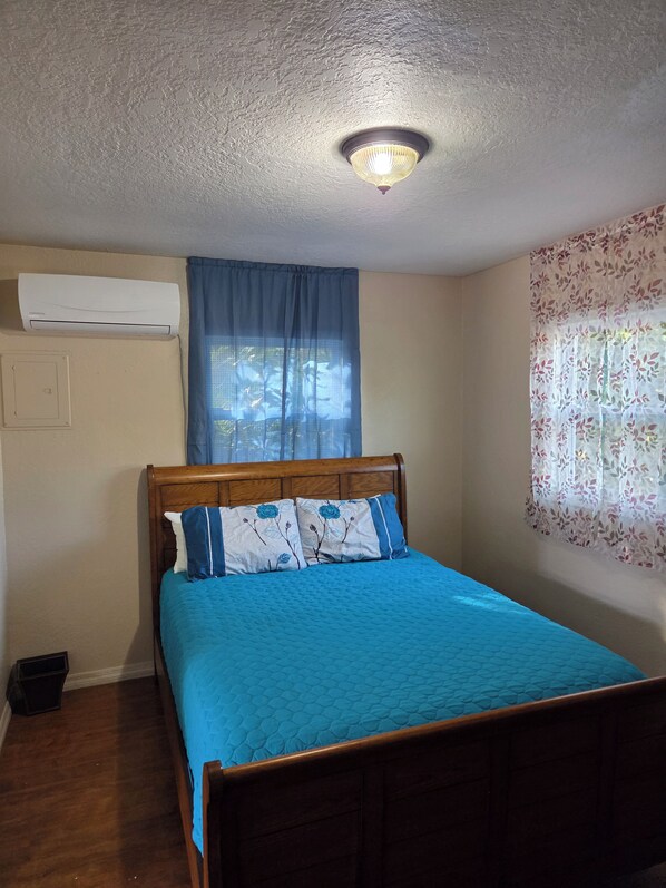 Quarto com cama, janela com cortinas florais, aparelho de ar condicionado e luminária no teto.