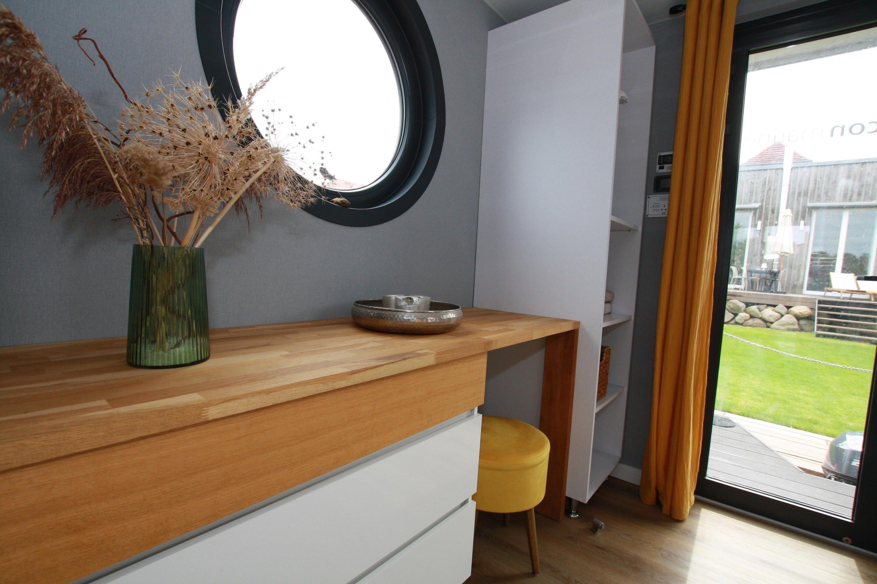 Eine moderne Küche mit einer Holz Arbeitsplatte, einem runden Spiegel und einer Vase mit Trockenpflanzen.