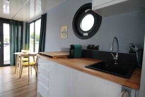 Una cocina compacta con un lavamanos, una cafetera y un pequeño comedor con una silla y una mesa.