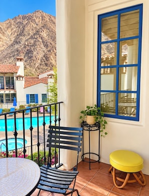 Ein Balkon mit Pool, einem Tisch, zwei Stühlen, einem gelben Hocker und einem Blumentopf.