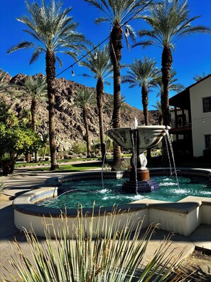 A pool area with a fountain, palm trees, and a mountainous backdrop. - A Charming Legacy Villa
3 bedroom 4 bath Steps to Pool & Stunning Mountain Views (La Quinta)