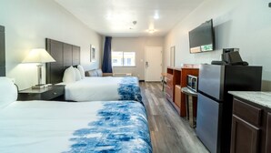 Ein Hotelzimmer mit zwei Betten, einem Schreibtisch mit Lampe, einer Mikrowelle, einem Kühlschrank und einem Fernseher an der Wand.