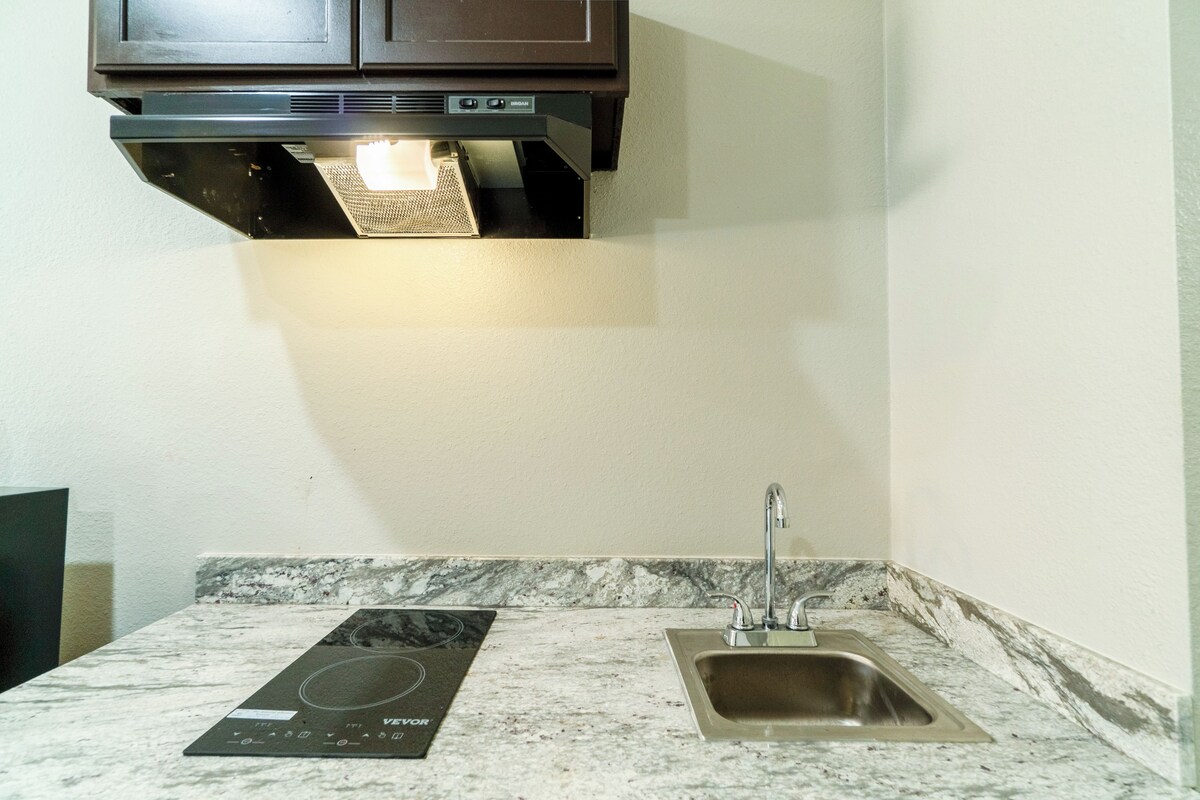 A kitchen with a built-in stove, a sink, and a dark-colored cabinet above the stove.