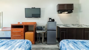 Een compacte hotelkamer met een bed, een bureau, een magnetron, een koelkast, een televisie en een kleine kitchenette.