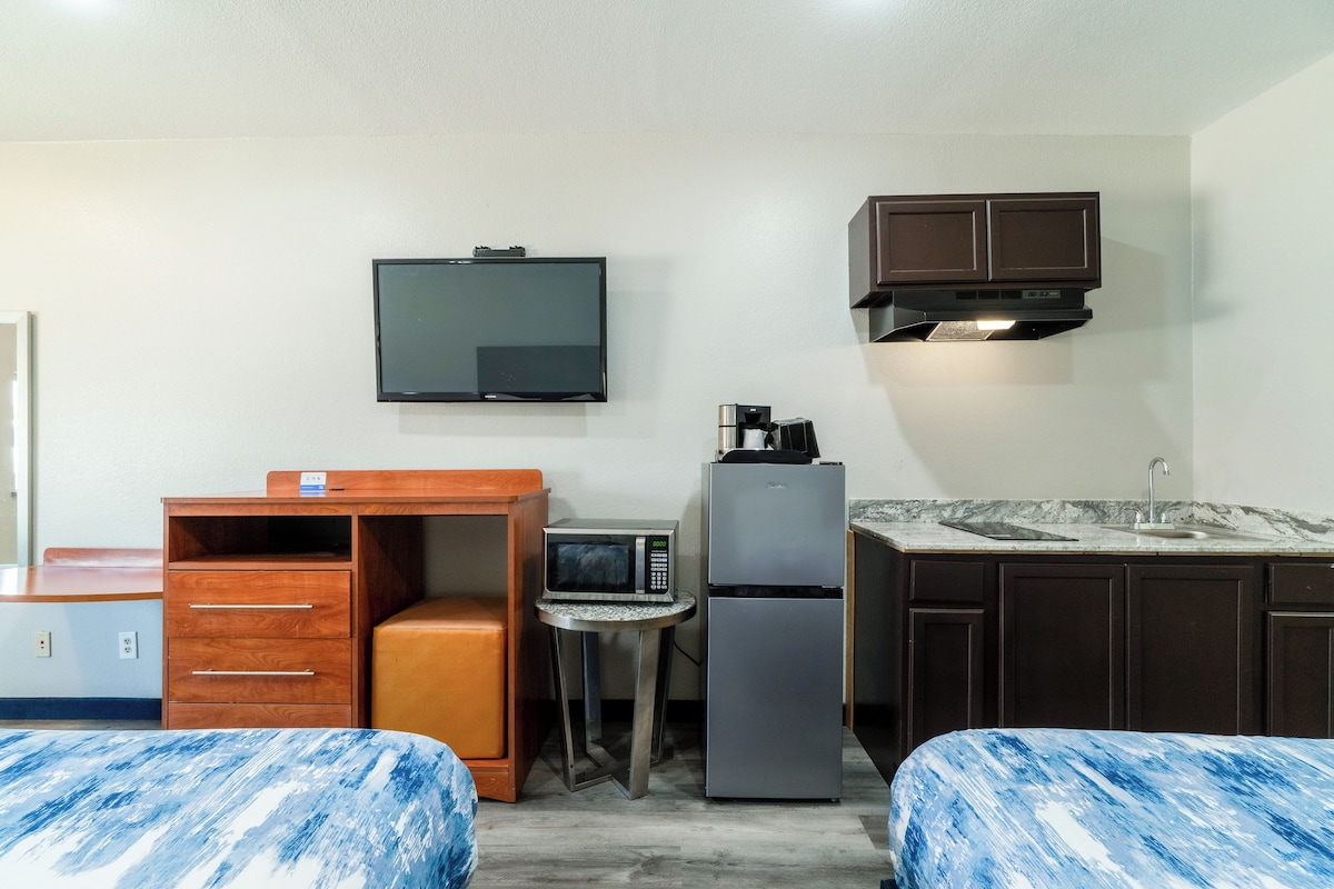 Una habitación de hotel compacta con cama, escritorio, microondas, refrigerador, televisión y una pequeña kitchenette.