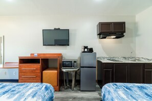 Una habitación de hotel compacta con cama, escritorio, microondas, refrigerador, televisión y una pequeña kitchenette.