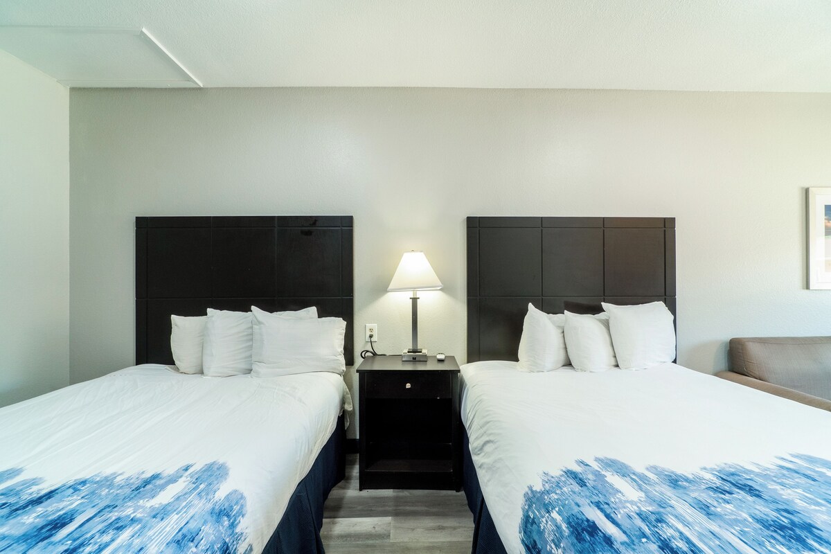 A hotel room with two beds, a nightstand with a lamp, and a framed picture on the wall.