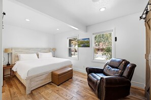 Une chambre à coucher avec un lit, un fauteuil en cuir, une fenêtre donnant sur un beau paysage et une lampe.