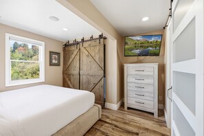 A bedroom with a bed, a wooden barn-style sliding door, a white dresser, and a large window with a view of trees. - Bea’s Canyon Lodge| Walk to Ski Trolley | Private Hot Tub | Sleeps 23 (Park City)