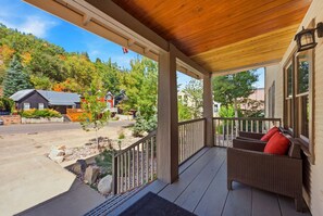 A covered porch with a view of a residential area, a stone pathway, and a wicker sofa with red cushions. - Bea’s Canyon Lodge| Walk to Ski Trolley | Private Hot Tub | Sleeps 23 (Park City)