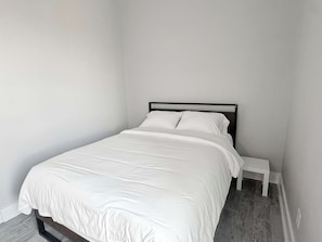 A single bed with a white mattress and pillows, a black metal frame, and a white bedside table in a room with plain white walls and a tiled floor. - Casa Dora Cove Beachfront (Bolivar Peninsula)