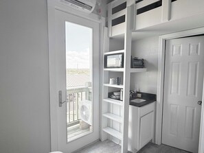 Ein kleines Badezimmer mit weißer Tür, einem integriertem Waschbecken und einem kleinen Fenster.