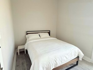 A single bed with a wooden frame and white bedding in a room with plain walls and a tiled floor. - Casa Dora Pearl Beachfront (Bolivar Peninsula)