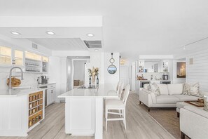 A modern kitchen with white cabinetry, a central island, and a dining area with a white sofa. - Naples Bay Waterfront Dolphins, Boat Dock & Pool (Naples)
