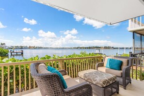 A balcony with wicker furniture, a view of the water, and a distant shoreline. - Naples Bay Waterfront Dolphins, Boat Dock & Pool (Naples)
