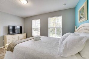 Ein Schlafzimmer mit einem Bett, einem Fernseher auf einer Kommode und zwei Fenstern.