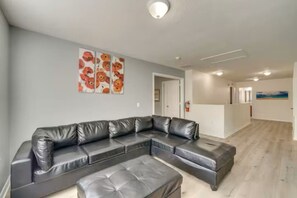 A modern living room with a sectional sofa and a matching ottoman, a hallway with a door, and a painting on the wall.