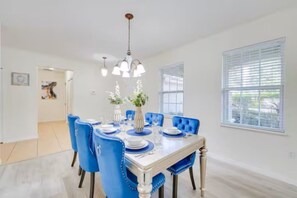 Een eetkamer met een witte tafel voor zes personen, blauwe gestoffeerde stoelen en een kroonluchter.