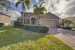 A residential house with a paved driveway, a garage, and well-maintained landscaping including grass and palm trees.