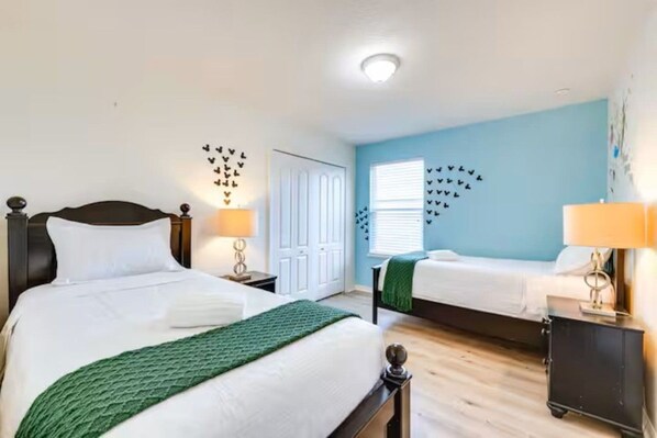 A hotel room with two beds, a wardrobe, a window with blinds, and wall decorations.