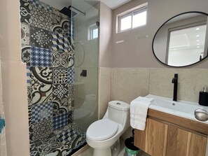Une salle de bain avec une douche carrelée, des toilettes, un lavabo avec un miroir et un porte-serviettes.