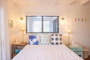 A bedroom with a bed, bedside tables, lamps, and a window with blinds. - Harbor View at Battery Hill •  Cruz Bay Views • Pool • Walk to Town & Beach (Saint John)