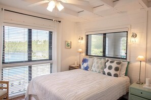 Ein Schlafzimmer mit einem Bett, zwei Nachttischlampen, einem Nachttisch, einem Fenster mit Jalousien und einem Deckenventilator.