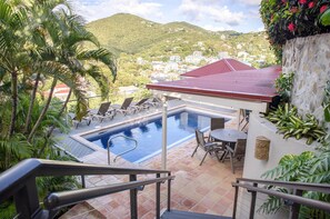 Ein Poolbereich mit Blick auf eine Hügelstadt, ein Gebäude mit rotem Dach und eine Treppe, die zum Pool führt.