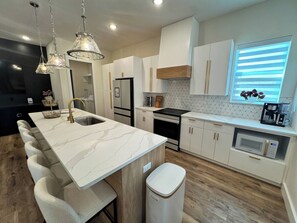 A modern kitchen with a marble countertop, stainless steel appliances, and pendant lighting. - Shell We Vacay 30A-Spacious 4 Bedroom - Private Saltwater Pool, PCB Florida (Panama City Beach)