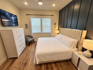 A bedroom with a bed, a dresser, a chair, a nightstand, a lamp, a window with blinds, and a painting on the wall. - Shell We Vacay 30A-Spacious 4 Bedroom - Private Saltwater Pool, PCB Florida (Panama City Beach)