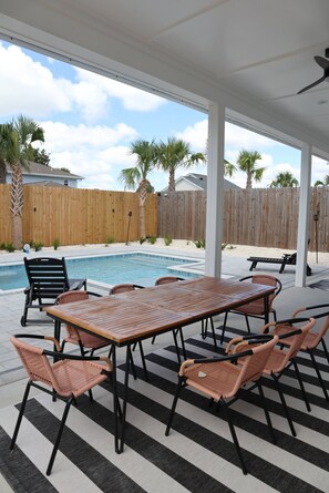 An outdoor patio with a pool, surrounded by a wooden fence, featuring a table and chairs. - Shell We Vacay 30A-Spacious 4 Bedroom - Private Saltwater Pool, PCB Florida (Panama City Beach)