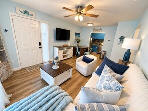 A living room with a ceiling fan, a television, a sofa, a chair, and a coffee table. - Coastal 2bd Condo with Community Pool and Hot Tub (Panama City Beach)