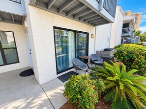 A modern building with a covered patio area, outdoor seating, and lush landscaping. - Coastal 2bd Condo with Community Pool and Hot Tub (Panama City Beach)