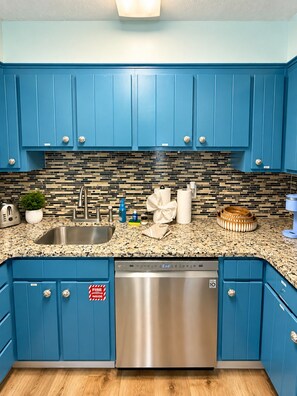 A kitchen with blue cabinets, a stainless steel dishwasher, and a tiled backsplash. - Coastal 2bd Condo with Community Pool and Hot Tub (Panama City Beach)