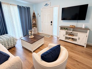 Un salon avec un canapé blanc, une table basse, un téléviseur et un meuble en bois.