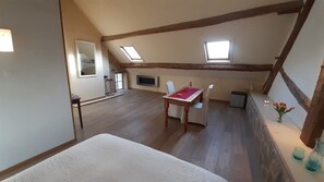 A room with a sloped ceiling, wooden beams, a dining table with chairs, a small window, and a radiator. - Holiday home 'Montgaudon' with beautiful views of the Morvan hills (Préporché)