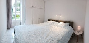 A bedroom with a bed, a nightstand, a lamp, and a window with curtains.