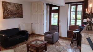 Ein Wohnzimmer mit Sofa, Sessel und Couchtisch, einem Gemälde an der Wand und Blick durch eine Tür.