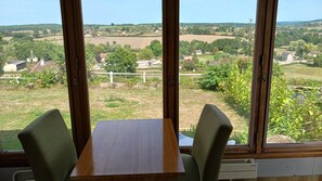 A room with a table and chairs, large windows with a view of a rural landscape.