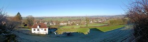 A rural landscape with a white house, green fields, and a distant town.